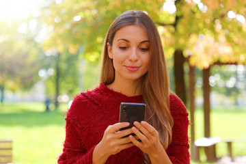 Close up of beautiful girl using internet browsing on smart phone on Autumn or Winter season.