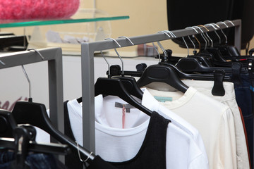 Various women's clothes are hung on black plastic hangers. Shop organization concept.