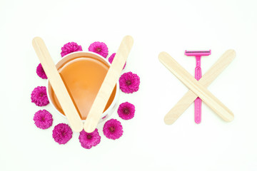 Flat lay top view of jar of wax with pink flowers vs razor for hair removal on white background....