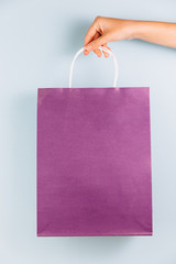 Female hand holding violet paper bag isolated on blue background