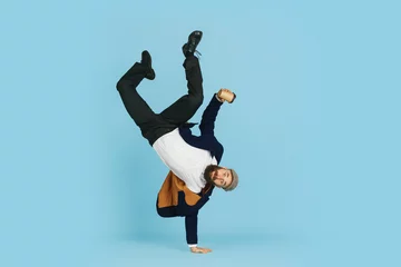 Tuinposter Young caucasian businessman having fun dancing break dance on blue studio background. Management, flexible, freedom, professional occupation, alternative way of modern working. Loves his job © master1305