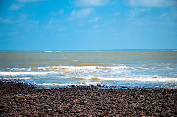 Vista da praia da Aruoca em Guimarães no Maranhão sem ninguém com pedras rochosas, ceu azul e águas em movimento
