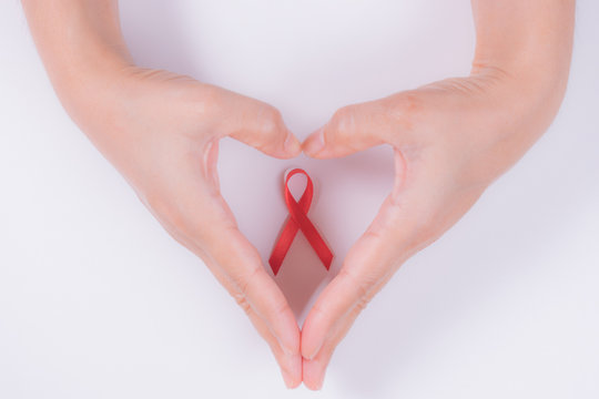 Woman hands forming a heart with her hands and a red ribbon for the fight against AIDS on a white background. - Powered by Adobe