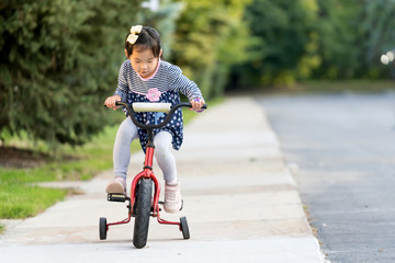 Cute little Asian girl learning ride a bicycle without wearing a helmet
