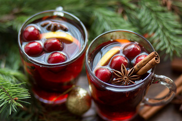 Mulled wine in glass mug with berries, cinnamon sticks and star anise on brown wood table