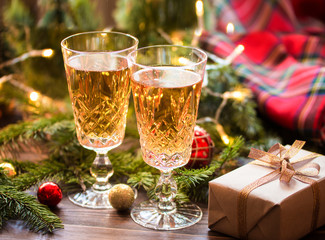 Two glasses of champagne on the wood table with gift box and christmas balls and fir branches. 