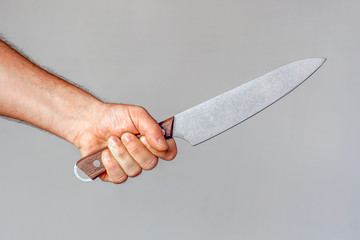 Hand of caucasian man holding a knife isolated on a gray background. Man hold knife - aggression. Big kitchen knife in man hand. Large kitchen knife in a man's hand.