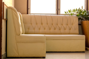 Old cream-colored sofa in the corner of the room with window light.