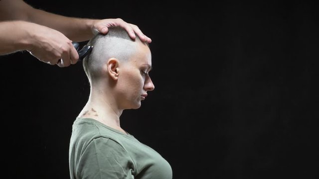 concept military girl. hands of a man hairdresser shave a woman's head bald, army hairstyle. Black background