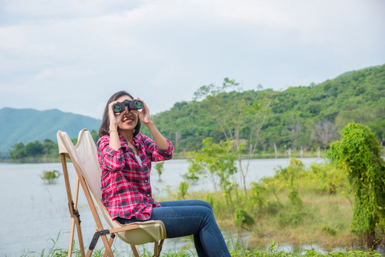 Beautiful Asian woman using binoculars to see the birds between camping at lake side camping site.
