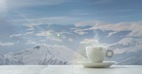 Single tea or coffee mug and landscape of mountains on background. Cup of hot drink with snowly look and cloudly sky in front of it. Warm in winter day, holidays, travel, New Year and Christmas time.