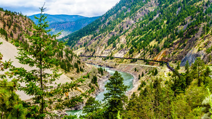 Fototapeta na wymiar Freight train on the railroad tracks running along the mighty Fraser River flowing in the Fraser Canyon in British Columbia, Canada