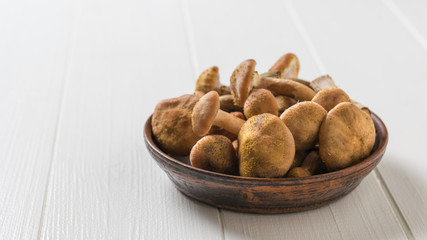 Clay bowl with forest mushrooms on a white table. Forest mushrooms on the table.