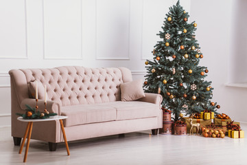 Beautiful beige sofa, Christmas tree with decorations and gifts, a table with candles. Cozy Christmas atmosphere. Stylish room interior with decorated Christmas tree.