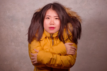 young beautiful Asian Chinese woman feeling cold and chilly freezing feeling cold in Winter weather wearing yellow jacket with fur hood isolated on grunge studio background © TheVisualsYouNeed