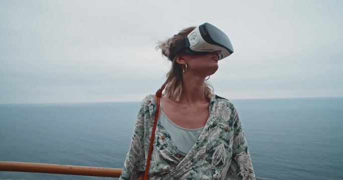 Blonde woman wearing VR headset staying at beautiful endless ocean. Modern girl experiencing virtual reality traveling to unique places. Black beach, Tenerife.
