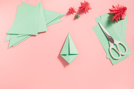 A process of making 3D fir tree from green paper on pink background. Step by step instruction, step 8. Turn over and fold right and left side to the centre line.