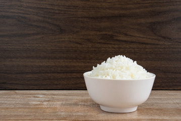 Cooked jasmine rice in white bowl on wooden table and dark background