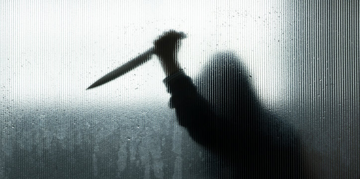 shadow of hand holding big sharp knife behind Frosted glass in the bathroom background.Robber,murderer or killer with knife.concept of scary crime scene of horror or thriller movies,Halloween theme