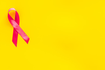 Pink ribbon as symbol of breast cancer awareness on yellow background top view space for text