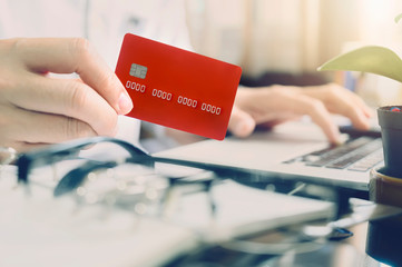 Closeup man hand holding red credit card while sitting at office desk in modern office.