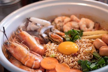 Spicy instant noodles soup(tom yum) with seafood shrimp squid Mussels sausage Pork Chops egg yolk in white pot