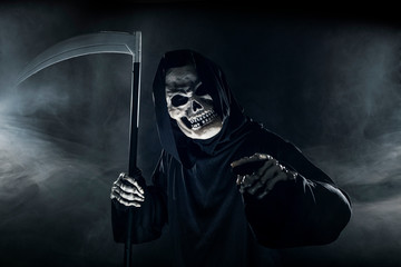 Scary looking grim reaper ghost wielding a scythe or sickle coming out of the fog.  The haunting...