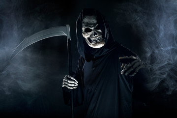 Scary looking grim reaper ghost wielding a scythe or sickle coming out of the fog.  The haunting...