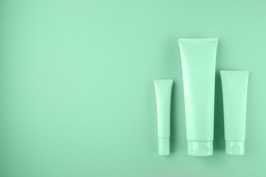 Collection of three cosmetic tubes on mint color background.