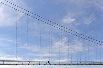 Obraz premium A bridge over a river with a man walking along it against a blue sky. Minimalism in the city.