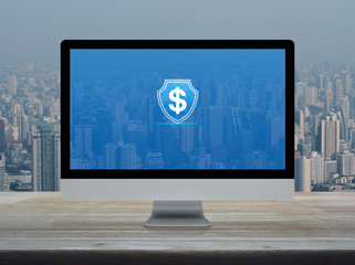 Dollar with shield flat icon on desktop modern computer monitor screen on wooden table over office building tower and skyscraper in city, Business money insurance and protection online concept