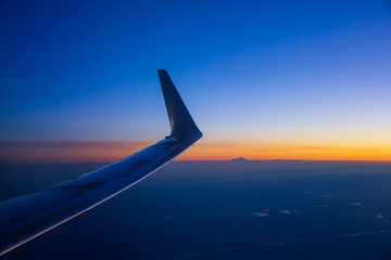 View of the wing of an airplane before dawn. Mountains and a peak are visible in the distance.