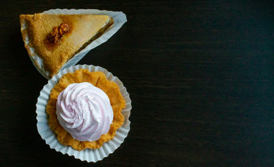 delicate dessert, a basket of light cream of light pink meringue and a nutty piece of cake on a dark wooden background.