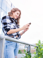 Pretty student girl in plaid shirt standing and looking at phone.