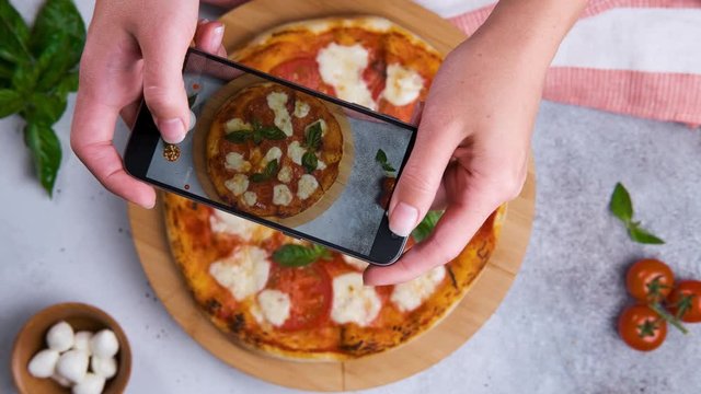 Technology, peoplem photo and food concept. Top view of woman hands taking picture of pizza with using smartphone.