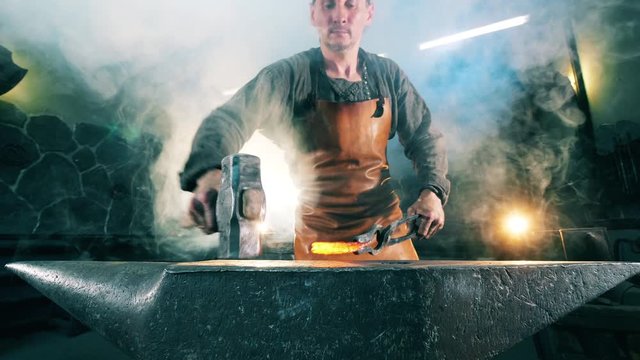 Working blacksmith shaping hot knife on anvil.
