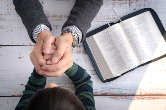 Top view closeup of a father and his little son's hands praying together after bible study in the morning. Christianity, Parenting and Raising child in God's way, Thankful moment, Happy father's day.