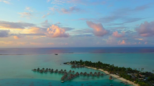 Aerial of scenic overwater bungalows on a stunning tropical island at dusk, drone flying forward then tilting down over the bungalows - Bora Bora, French Polynesia