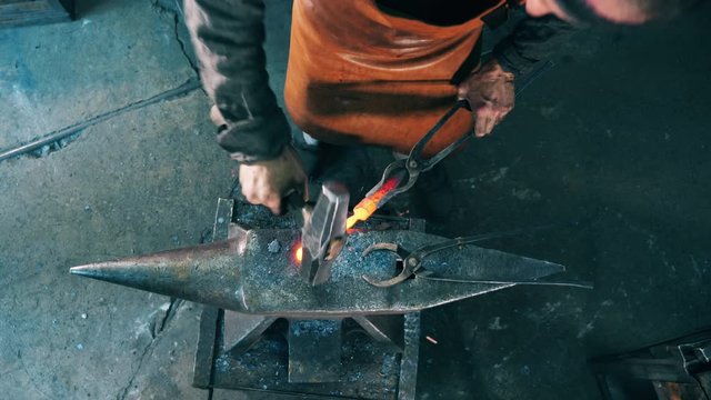 One blacksmith shapes knife on anvil, using hammer.