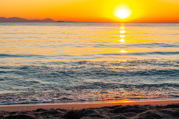 The sunset sun is going down behind the horizon. Tyrrhenian Sea bay with Elba island on the background at the sunset. Cala Violina beach