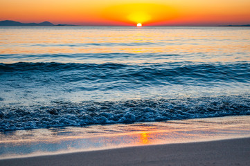 The sunset sun is going down behind the horizon. Tyrrhenian Sea bay with Elba island on the background at the sunset. Cala Violina beach