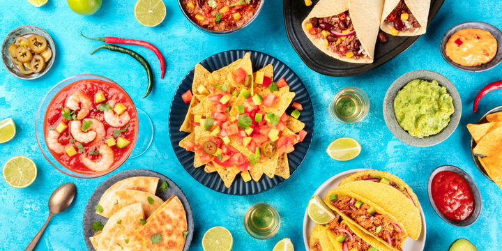 A Panorama Of Mexican Food, Many Dishes Of The Cuisine Of Mexico, Flat Lay, Top Shot On A Blue Background. Nachos, Tequila, Guacamole, Quesadillas, Shrimp Cocktail, Taco Shells