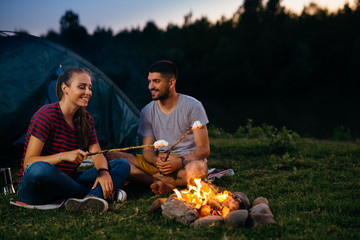 romantic couple on camping by the camping fire toasting marshmallows