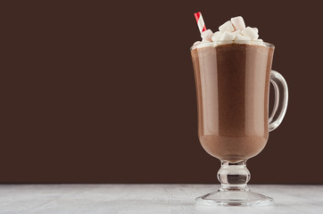 Season hot chocolate milk cocktail with marshmallows and red striped straw in elegant dark brown bar interior, copy space.