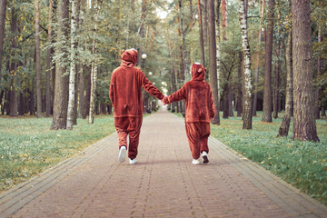 couple in bear costumes hold hands. young guy and girl walk along the road together.