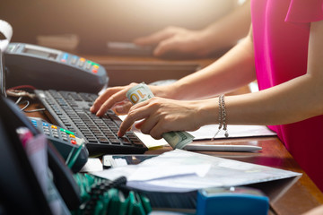 hands of a female manager at the hotel reception. The woman is holding a hundred dollars and typing something on the keyboard