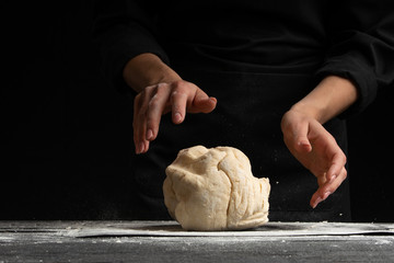 Pastry chef or baker cooks dough with flour, for sweets, rolls or Italian pizza or pasta. On a black background for design, for advertising or a signboard on a bakery, bakery banner
