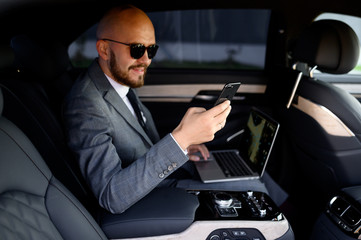 handsome businessman using his mobile phone in a modern car with a driver in center of the city....