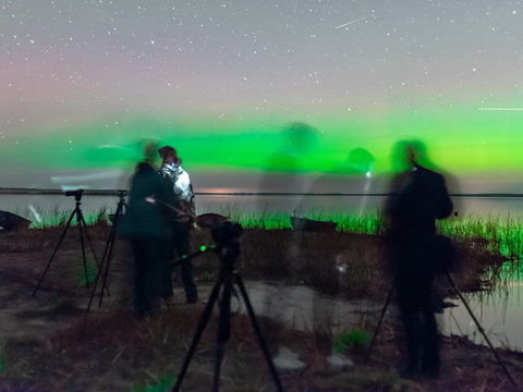 picture with a northern lights on the lake, blurred background.  fuzzy and moving human silhouettes in the foreground