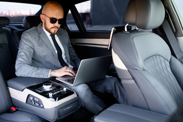 handsome businessman using his mobile phone in a modern car with a driver in center of the city. Concept of business, success, traveling, luxury 